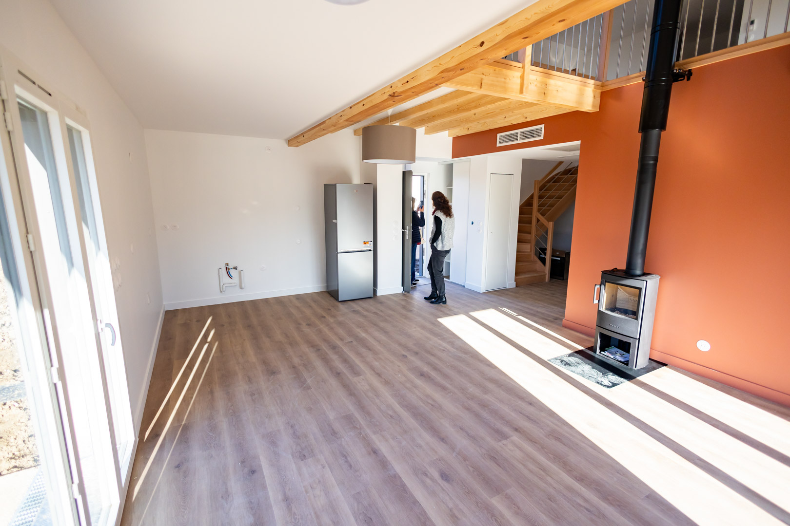 Grande pièce à vivre avec mur terracotta, poêle à bois et mezzanine en bois